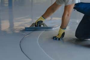 Close-up of a man wearing gloves carefully spreads epoxy resin across a concrete floor for a home improvement project.