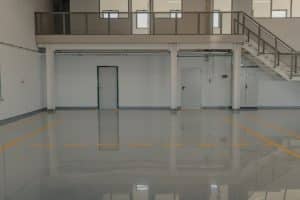 A large empty room with a staircase in the background. The floor appears to be made of concrete, but chemical resistant epoxy flooring is a popular choice for garages due to its durability and resistance to spills