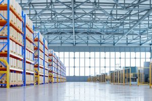 Modern industrial warehouse with epoxy flooring for industrial use, featuring high ceilings, extensive shelving units stocked with boxes, and advanced machinery. The image showcases the slip-resistant and durable qualities of epoxy flooring in industrial workplaces.