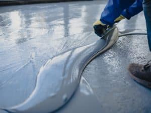 Worker applying epoxy outdoor flooring, demonstrating the smooth finish and highlighting the long-term benefits for durability and aesthetics.