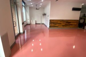 modern commercial space featuring pink interior epoxy flooring, wood accent wall, large windows, and ceiling fan for a stylish look