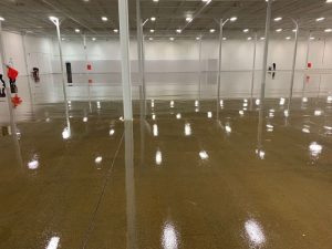 Shiny warehouse floor with epoxy coating on floor, reflecting overhead lighting and structural support columns.