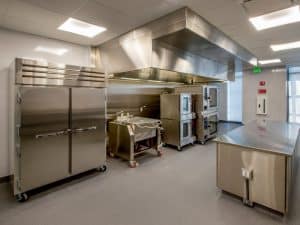 Large commercial kitchen featuring durable stainless steel counters and epoxy finish floor for easy cleaning and safety.