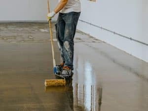 Worker applying an epoxy floor coating, demonstrating epoxy flooring durability and its smooth, protective finish during installation.