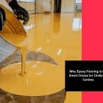 Worker pouring yellow epoxy resin onto a floor during installation of child friendly flooring in a childcare centre.