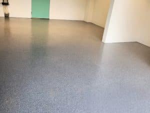 Empty art space featuring seamless grey flake epoxy art gallery flooring with clean white walls and a mint-green door.
