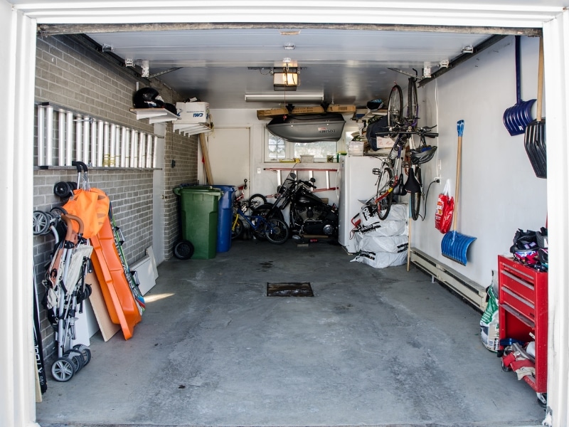Cluttered single garage without epoxy floor, exposed concrete surface.