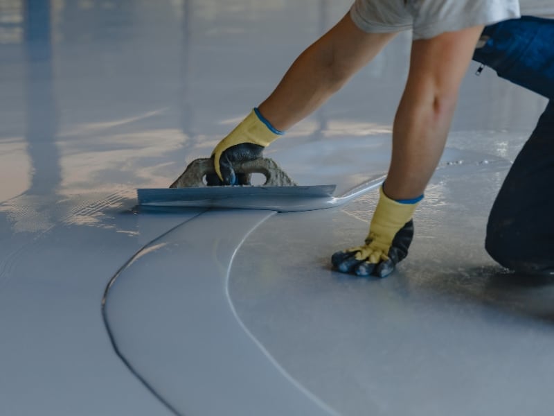 Worker smoothing floor coating with trowel to show epoxy flooring installation cost process